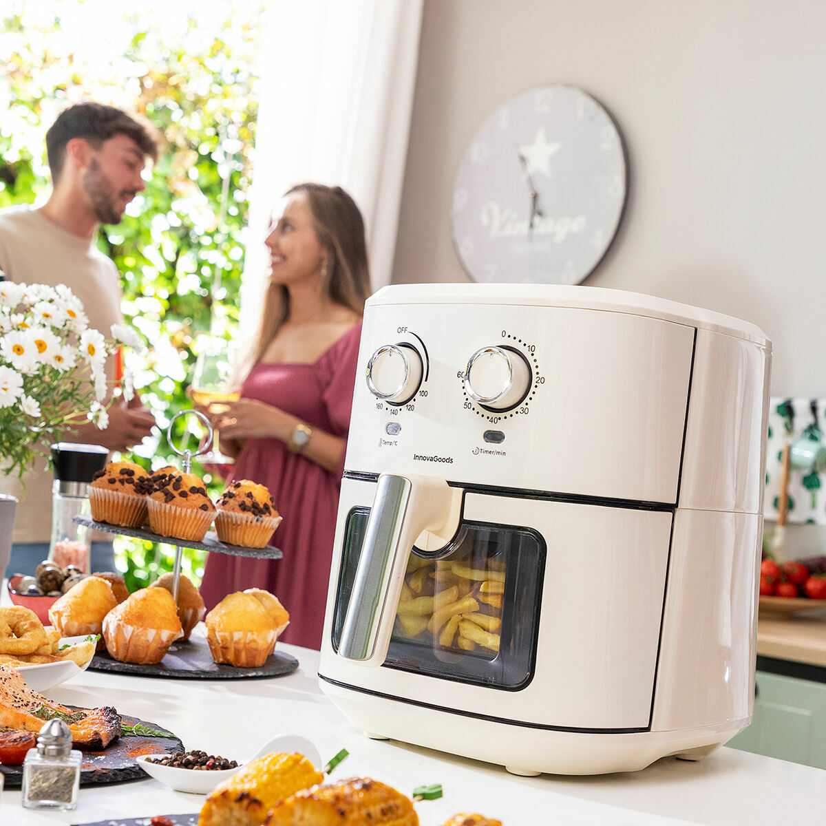 White air fryer on a kitchen counter with people and food in the background
