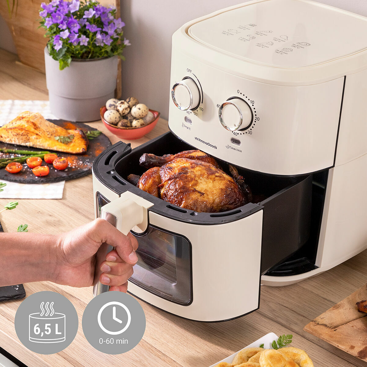 Person using a white air fryer with food inside on a wooden table.