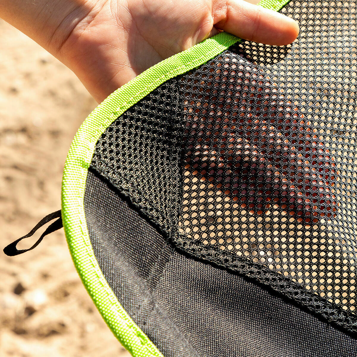 Close-up of a hand holding a black mesh bag with green trim.