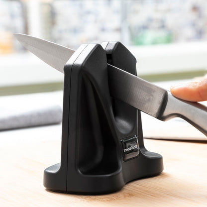 Knife sharpener with a knife being sharpened on a wooden surface.