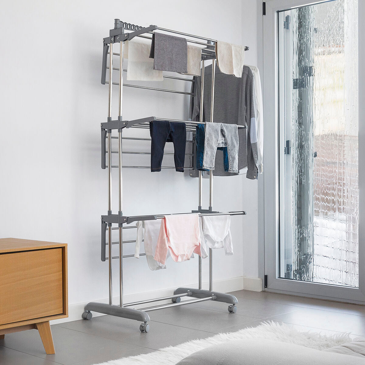 Clothes drying rack with clothes in a room with a sliding glass door.