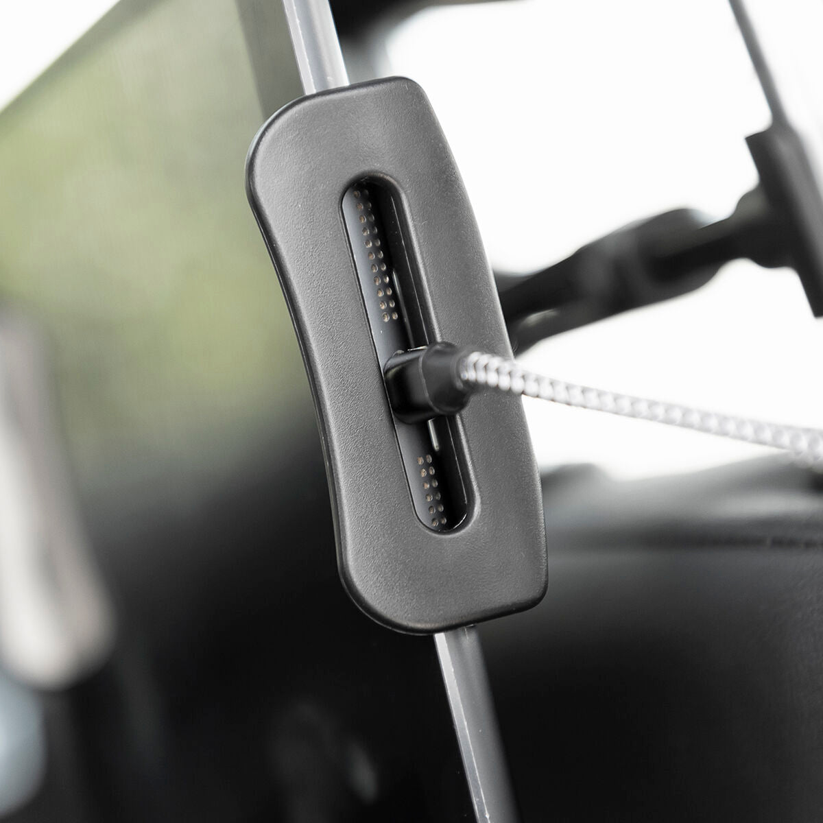 Car visor with a mounted device, possibly a phone holder or camera, with a blurred interior background.