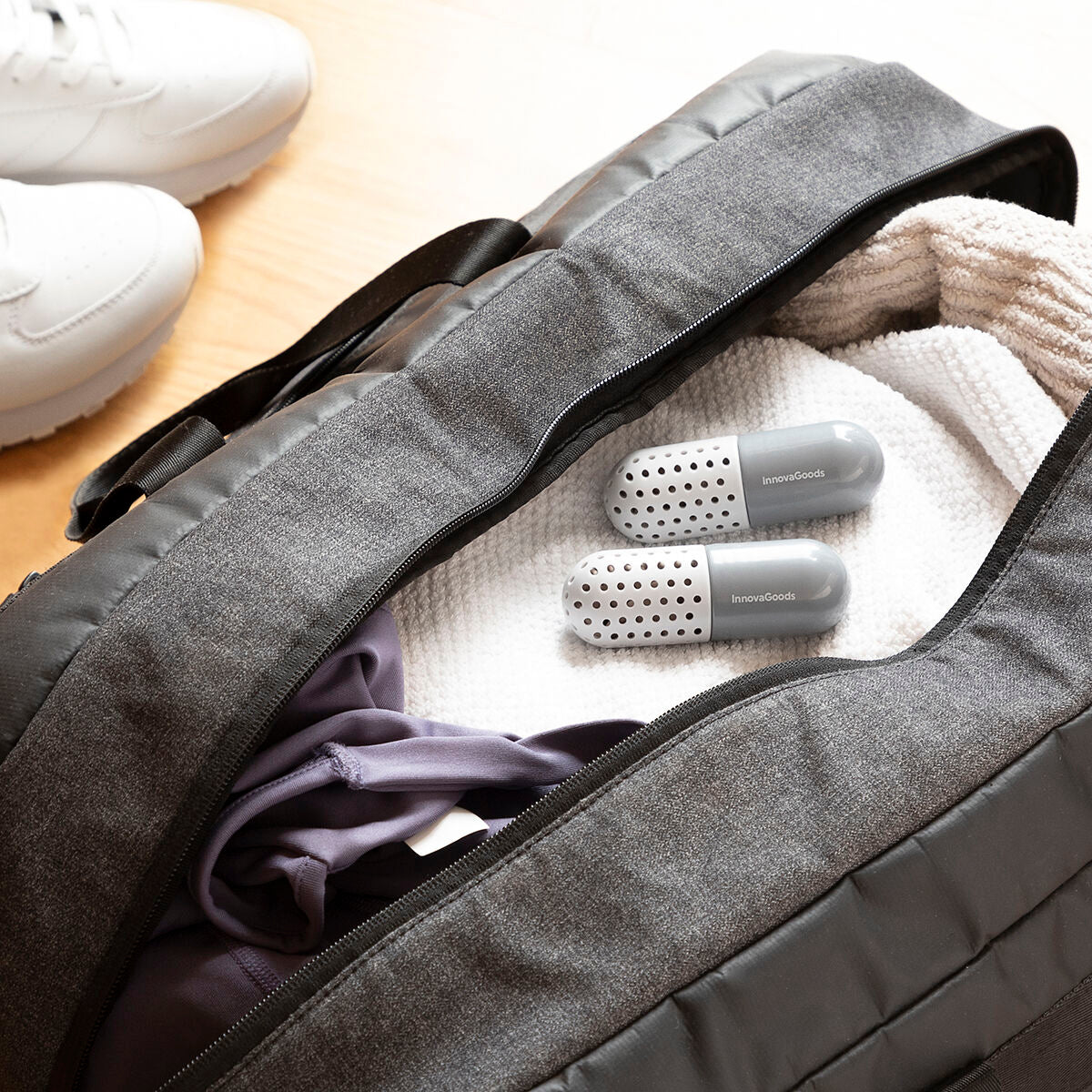 Gray travel bag with clothes and two gray hairbrushes on a wooden surface.