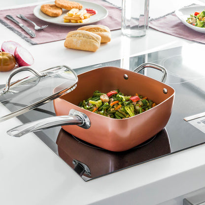 Copper cookware with vegetables on a stove, surrounded by a dining setup.