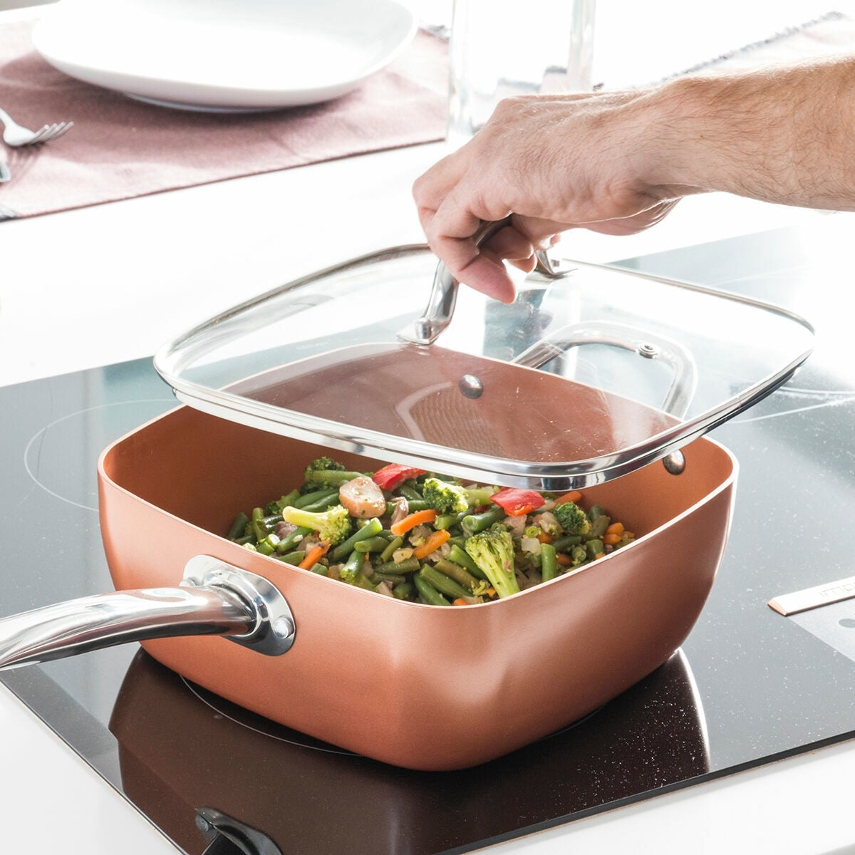 Copper cookware with vegetables on a stove, hand placing a lid on.