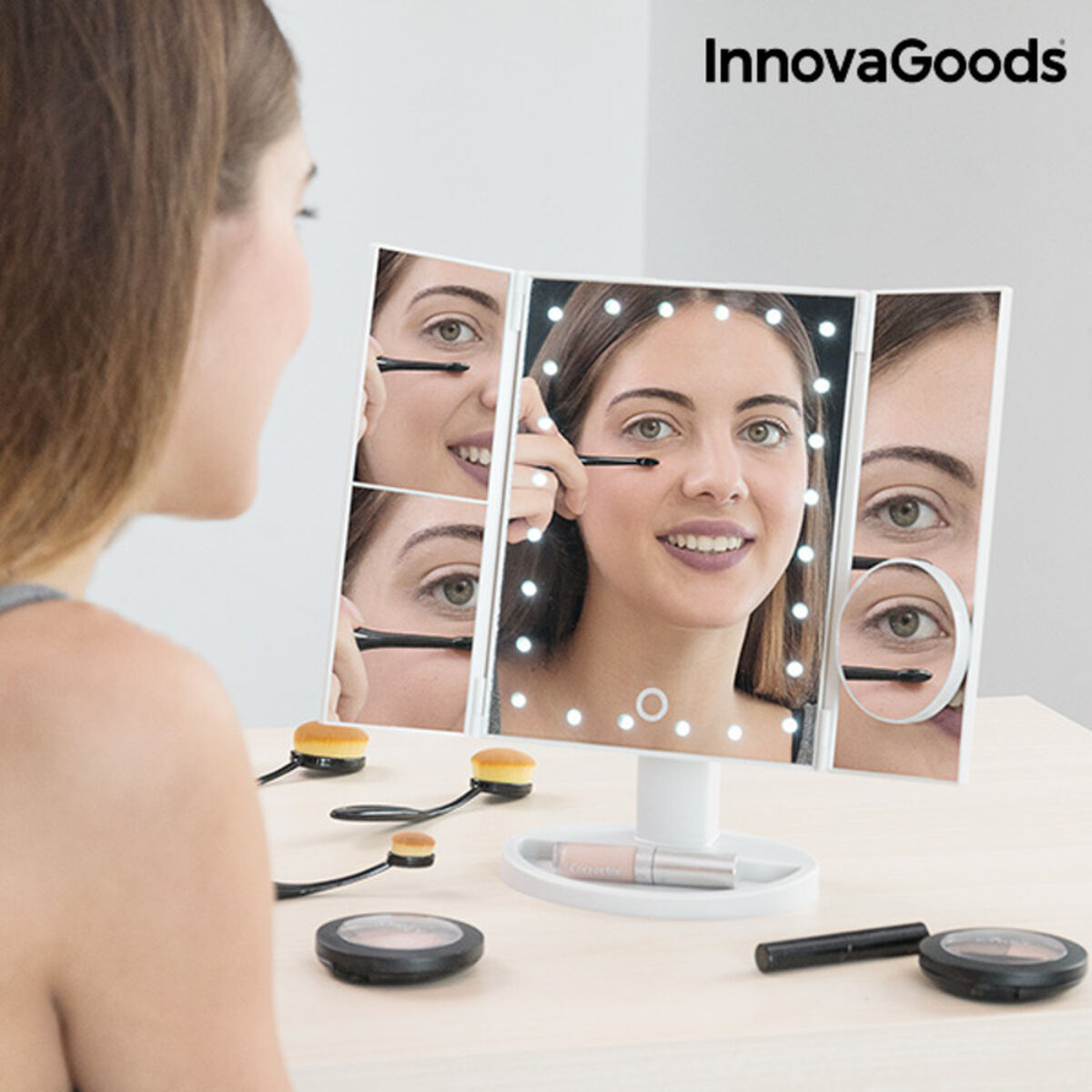 Woman using a makeup mirror with LED lights andinnovaGoods branding.