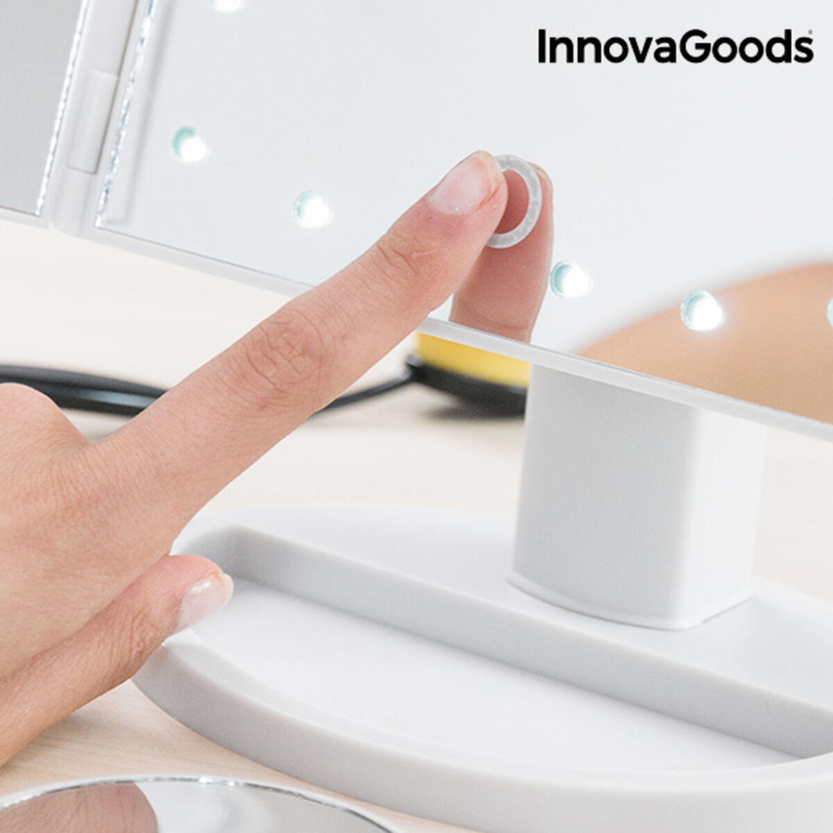 Hand pressing a small white button on a white electronic device with 'InnovaGoods' branding.