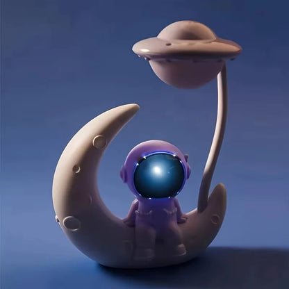 Toy figure of an astronaut on a moon with a UFO above, against a blue background